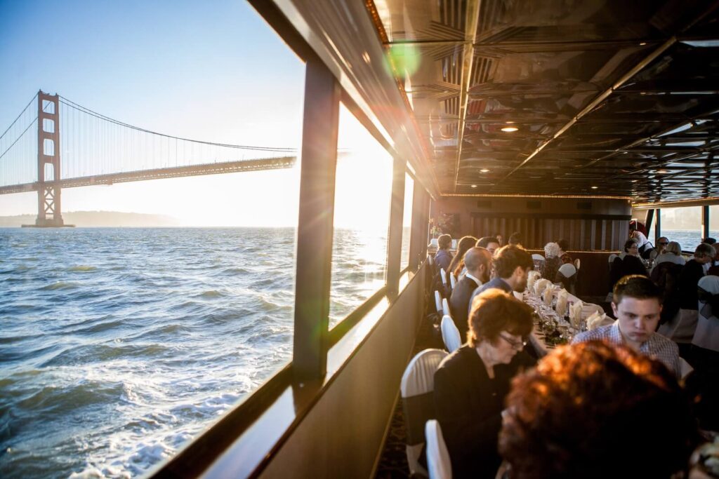 Cruise ship at sunset under the Golden Gate Bridge with guests dining.