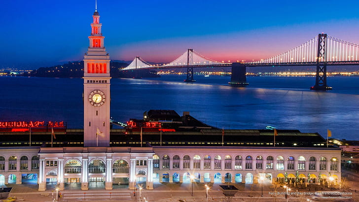 View of the Ferry Building and Bay Bridge lit up at night.